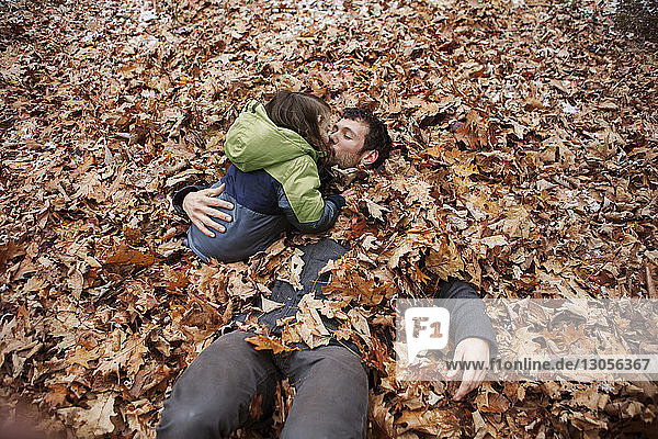Hochwinkelaufnahme eines Vaters  der seinen Sohn küsst  während er im Laub liegt