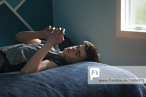 Junge benutzt Mobiltelefon  während er zu Hause im Bett liegt