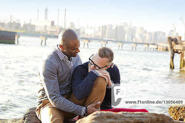 Romantic boyfriends while sitting on rocks against river