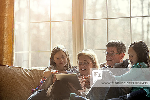 Großeltern benutzen Tabletten  während sie mit Kindern zu Hause auf dem Sofa sitzen
