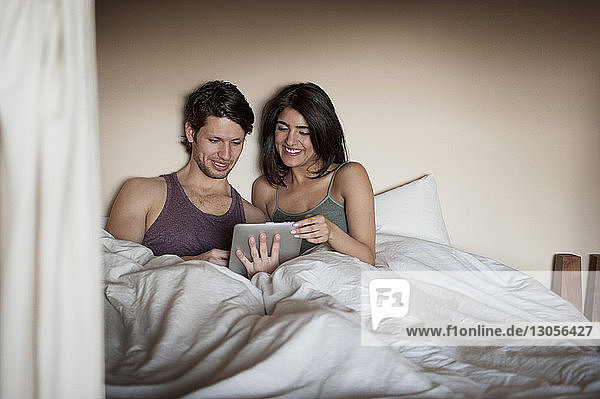 Cheerful young couple looking at digital tablet on bed