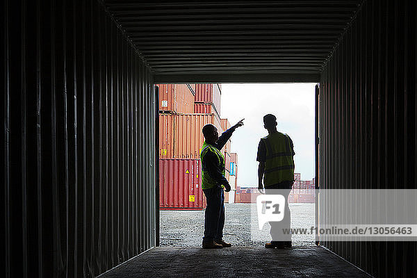 Worker pointing away while standing with man by cargo container at commercial dock