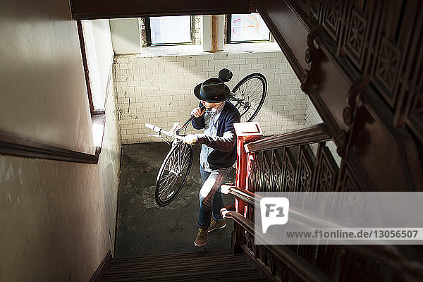 Hochwinkelansicht eines Mannes  der zu Hause beim Treppensteigen ein Fahrrad trägt