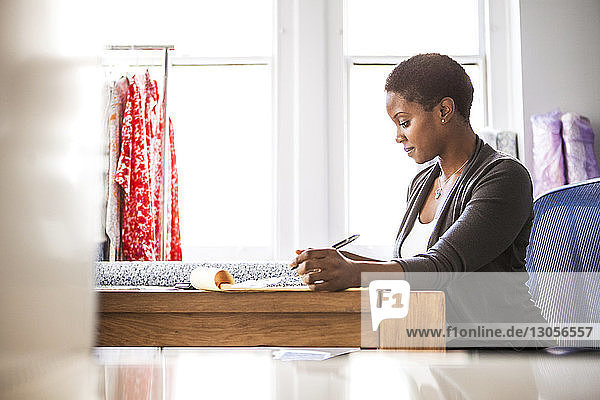 Side view of female fashion designer working on desk against window