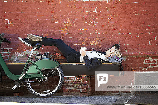 Frau liegt auf Bank mit geparktem Fahrrad an Wand