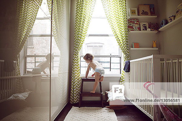 Mädchen klettert zu Hause am Fenster auf einen Hocker