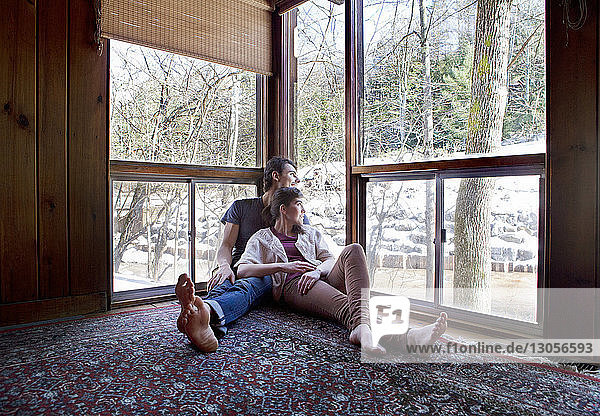 Couple looking through window while sitting at home