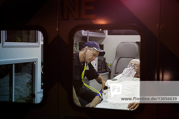 Rettungshelfer untersucht Patient mit Stethoskop im Krankenwagen