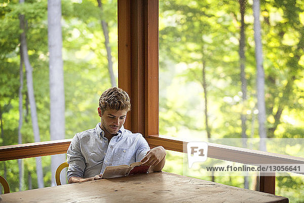Boy reading book while sitting on chair by table