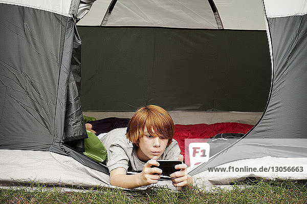 Junge benutzt Telefon  während er vorne im Zelt liegt