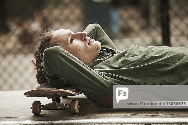 Seitenansicht eines Mannes  der sich mit dem Kopf auf ein Skateboard lehnt  im Skateboard-Park