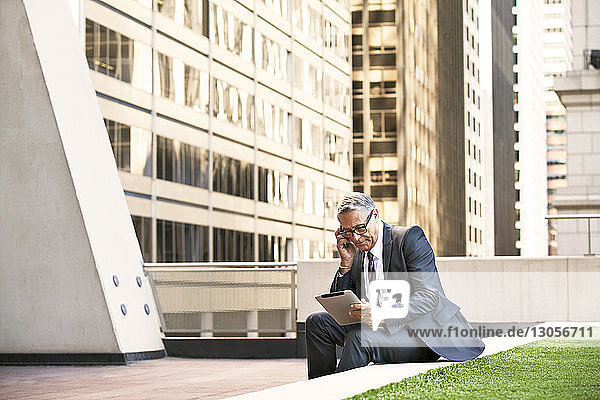 Geschäftsmann hält Tablet-Computer in der Hand  während er auf einer Stützmauer sitzt