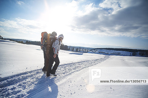 Freunde tragen Rucksack beim Wandern auf schneebedecktem Feld gegen bewölkten Himmel