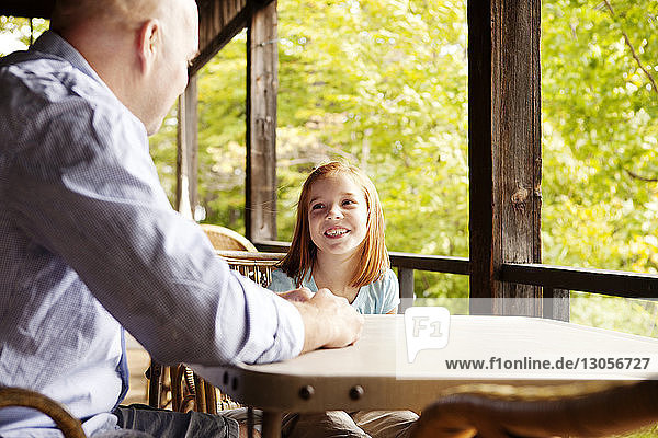 Glückliches Mädchen unterhält sich mit dem Vater  während sie im Pavillon am Tisch sitzt