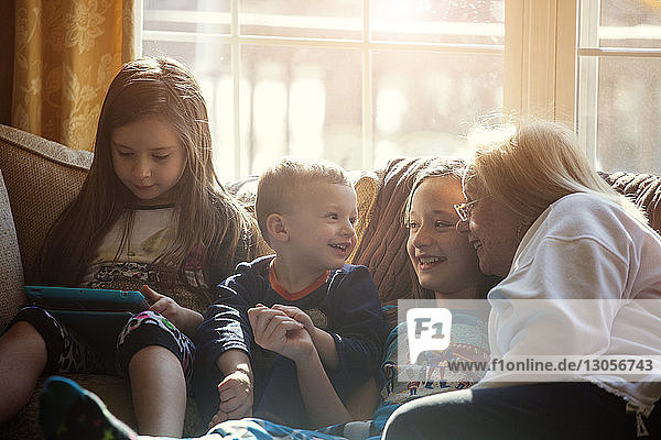 Happy children sitting with grandmother on sofa at home