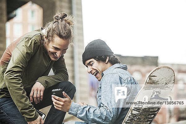 Happy friends looking at smart phone in skateboard park