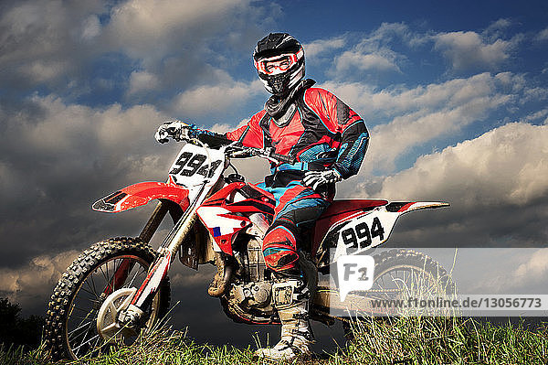 Porträt eines selbstbewussten Motorradfahrers auf dem Feld vor bewölktem Himmel in voller Länge