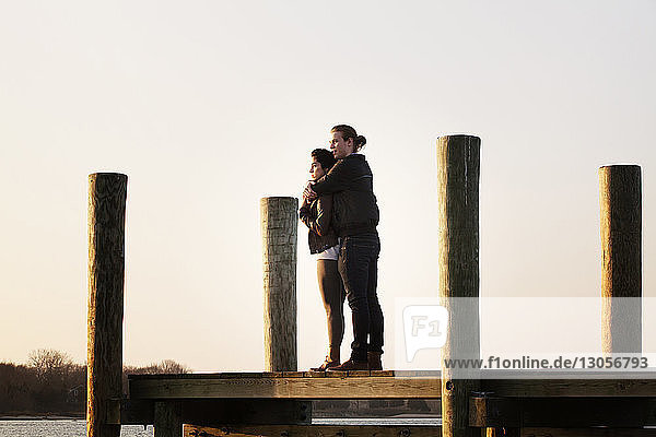 Couple standing on pier against sky during sunset