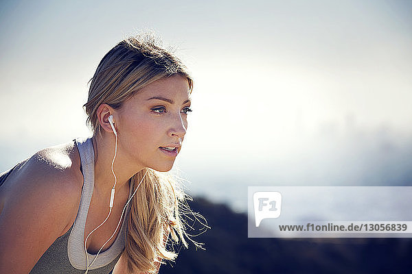 Woman listening music through headphones against sky