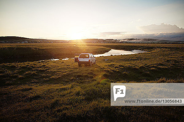 Car parked on field by river during sunset