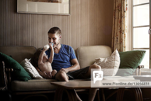Playful son feeding father while sitting on sofa at home