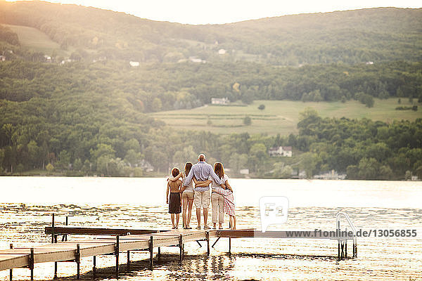 Rückansicht einer Familie  die auf dem Steg über dem See die Arme umkreist