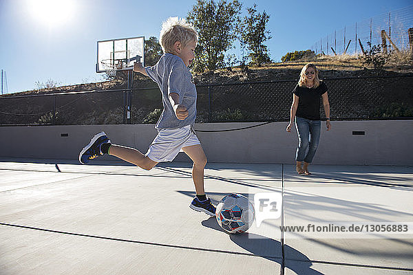 Junge kickt Ball beim Fussballspielen mit der Mutter