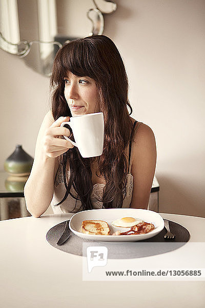 Frau schaut weg  während sie zu Hause Kaffee bei Tisch trinkt