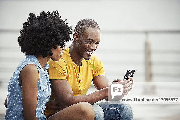Couple looking at mobile phone while sitting on promenade