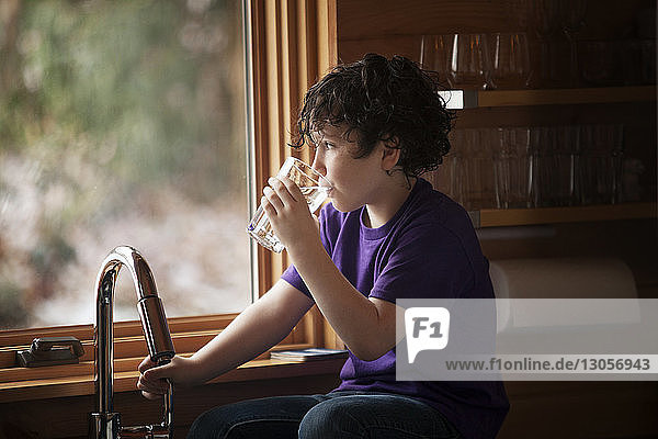 Junge trinkt Wasser  während er zu Hause an der Küchentheke sitzt
