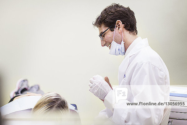 Lächelnder Zahnarzt schaut den Patienten an  während er in der Klinik sitzt