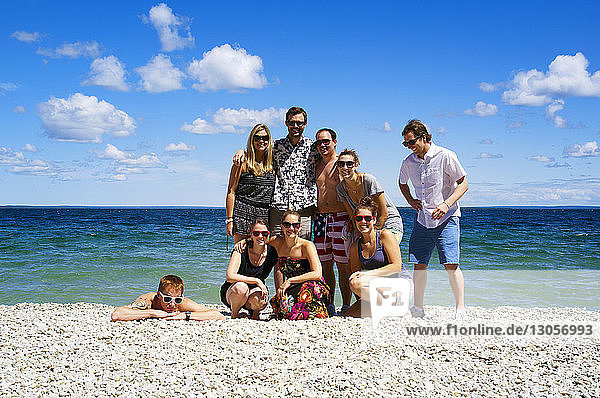 Portrait of happy friends standing on beach during sunny day