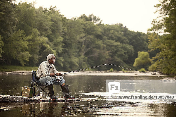 Man fishing while sitting on chair at lake
