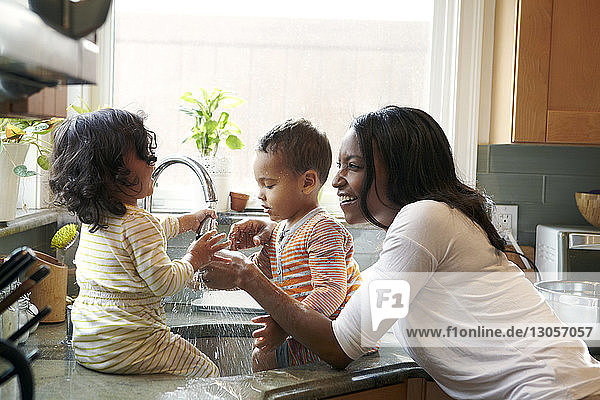 Mother looking at children playing with water in sink at kitchen