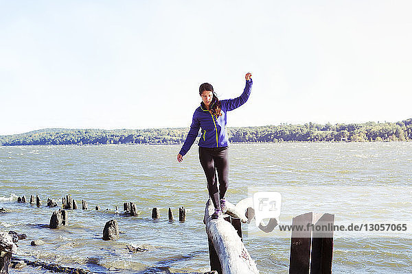 Frau balanciert auf Baumstamm über Fluss gegen klaren Himmel