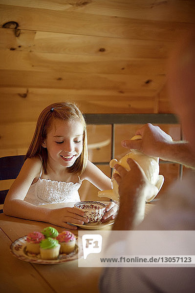 Ausgeschnittenes Bild eines Vaters  der einer glücklichen Tochter Tee serviert  während er am Tisch sitzt