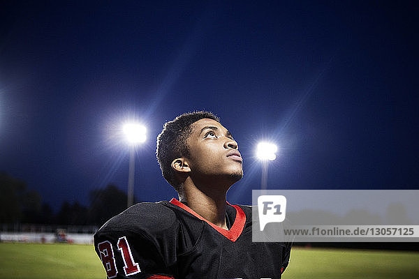 Nahaufnahme eines jugendlichen American-Football-Spielers  der auf ein beleuchtetes Spielfeld schaut