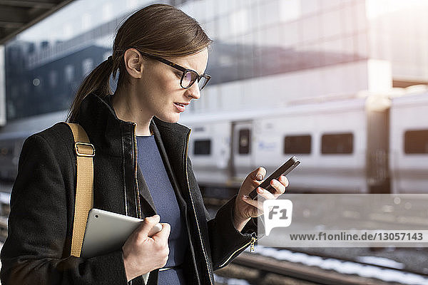 Junge Geschäftsfrau versendet Textnachrichten  während sie am Bahnhof steht