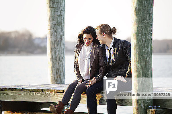 Glückliches Paar sitzt bei Sonnenuntergang am Pier