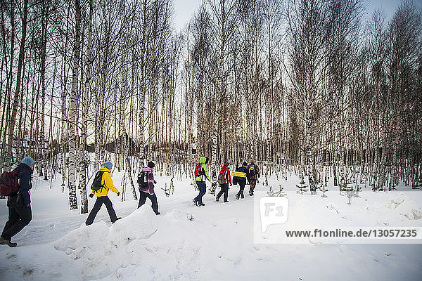 Hikers walking on snow covered field against bare trees