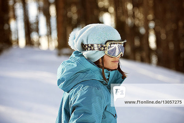 Frau mit Skibrille steht auf verschneitem Feld