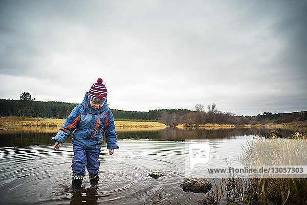 Boy standing on river against cloudy sky