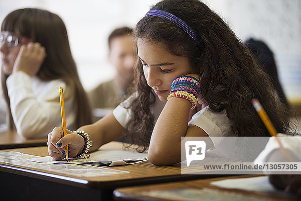 Schulmädchen schreibt Test  während sie im Klassenzimmer am Schreibtisch sitzt