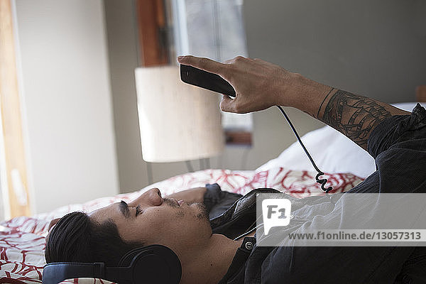 Junger Mann hört Musik  während er zu Hause im Bett liegt