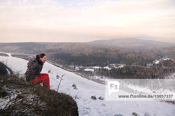 Woman sitting on mountain against sky during winter