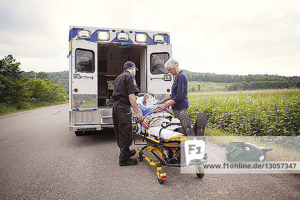 Patient liegt auf Krankenhausbahre von Sanitäter und Ehefrau auf Straße stehend