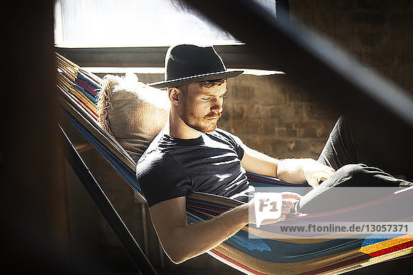 Mann liest Buch  während er sich zu Hause in der Hängematte entspannt