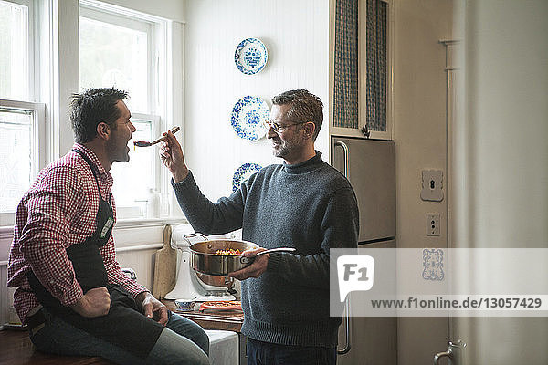 Mann füttert Freund  der zu Hause auf dem Küchentisch sitzt