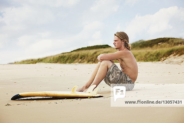 Man with surfboard sitting on sand at beach