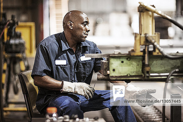 Man working while sitting by machinery in metal industry